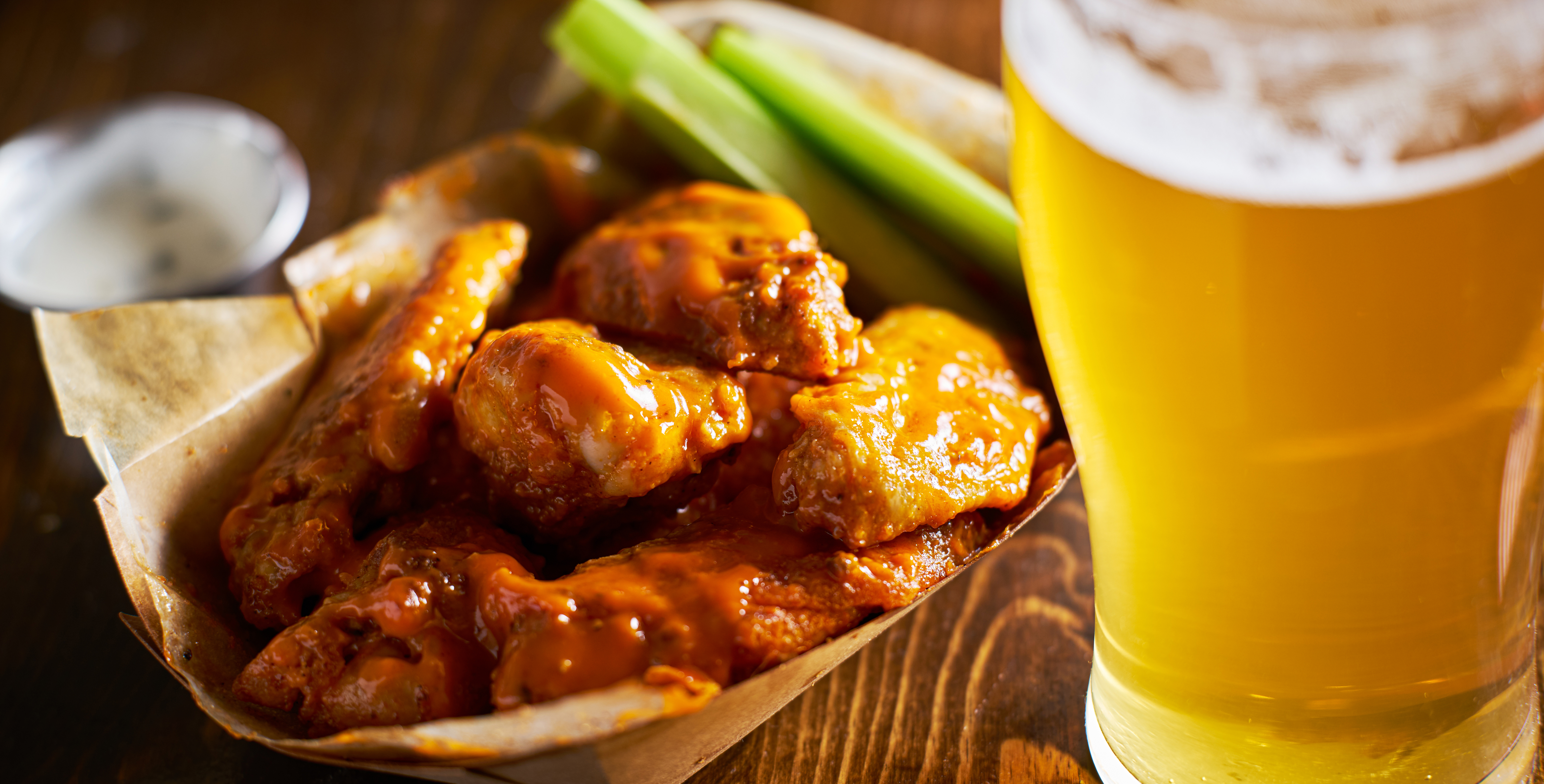 pale ale in a pint glass in front of a serving of hot wings and celery