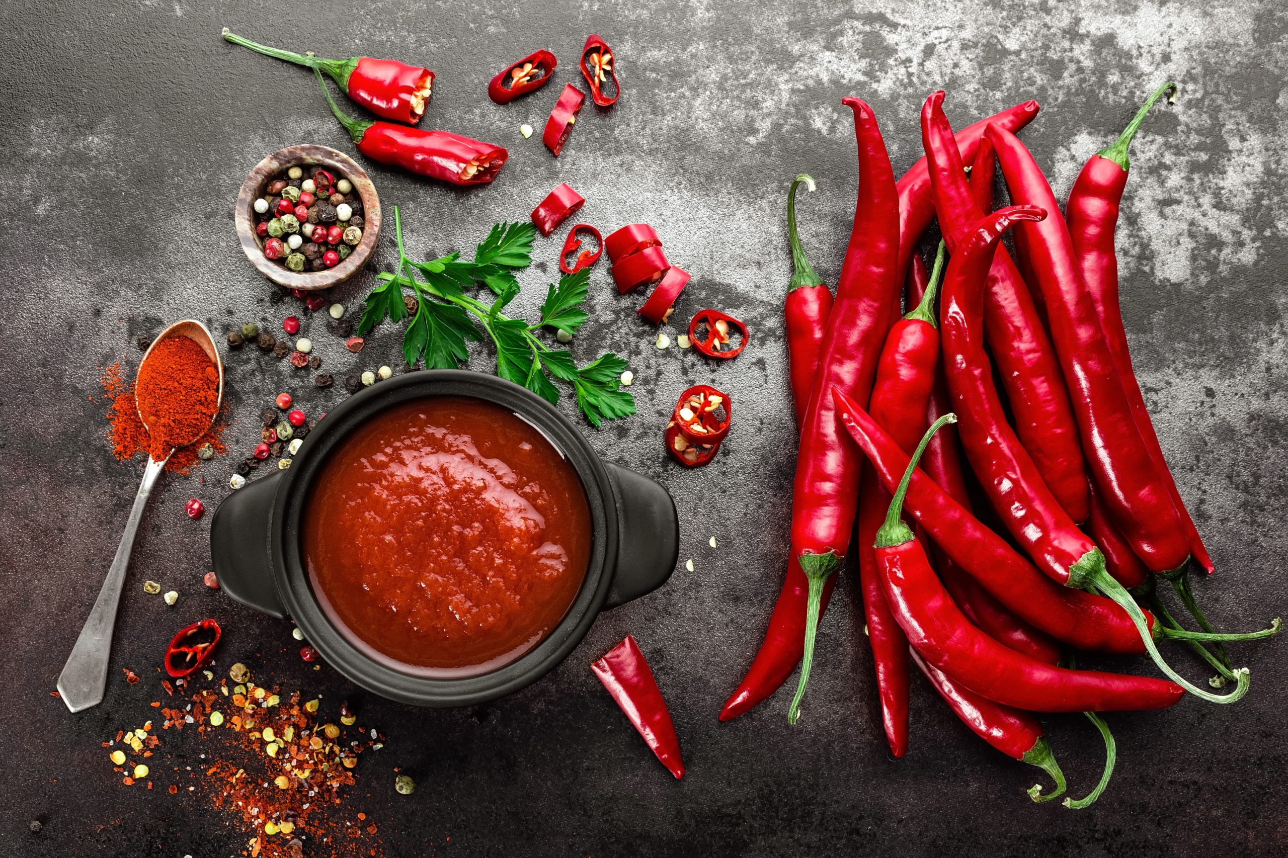 overhead shot of a ramekin of spicy red sauce aside some chili peppers